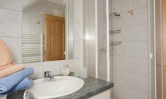 A modern bathroom with a shower and a sink. White tiles and beautiful towels create a bright, welcoming atmosphere.