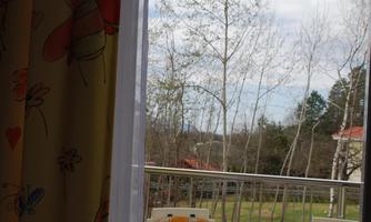 A beautiful balcony with a round table and two chairs in yellow and white. In the background, there are trees and a cloudy sky.