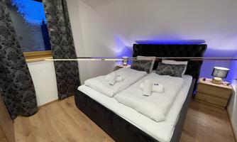 A modern bedroom with a double bed and elegant lighting. The curtains are dark and the floor is wooden.