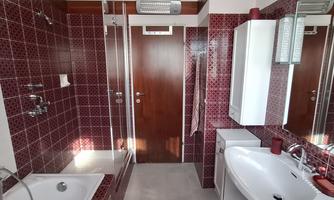 A modern bathroom with red patterned tiles and a bathtub. There is a shower, a large mirror, and bright lighting.