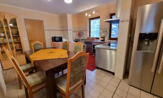 A cozy kitchen with a large table and chairs. In the background, there are kitchen cabinets and a modern stove.