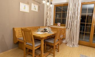 A cozy dining area with a wooden table and chairs. The windows are adorned with curtains and there is art on the walls.