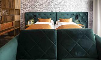 A modern bedroom with two single beds and an elegant wall cladding. In the foreground is a green sofa that creates a cozy atmosphere.