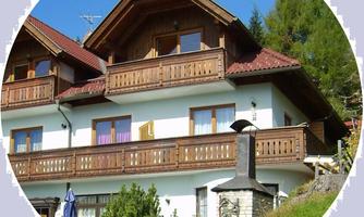 A charming wooden house with several balconies and a green lawn in front of it. In the background, there are trees and a blue sky.