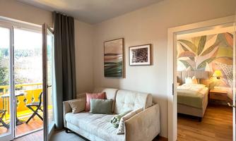 A bright living room with a cozy sofa bed and a carpet. Through the terrace door, you access a balcony with a view of the greenery.