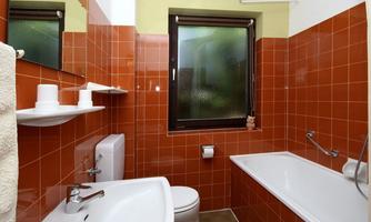 A bathroom with orange tiles, a bathtub, and a toilet area. There is also a sink with a mirror and shelves.