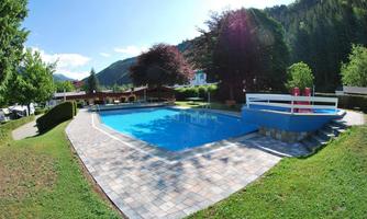An inviting swimming pool surrounded by grassy areas and trees. The sunny atmosphere creates a relaxed holiday vibe.
