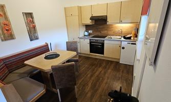 A modern kitchen with wooden cabinets and a dining table. The atmosphere is friendly and inviting.