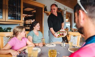 A waiter serves a delicious dish at a table with guests. The atmosphere is friendly and inviting.