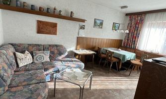 A cozy living room with a large couch and a dining table. The room is brightly lit and has a rustic decor.