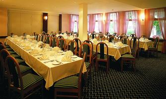 An elegant dining room with long tables that are beautifully set. The windows are adorned with curtains, and there is plenty of light.