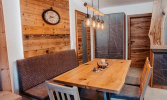 A cozy dining area with a large wooden table and a bench. The walls are clad in wood, and stylish lamps hang above the table.