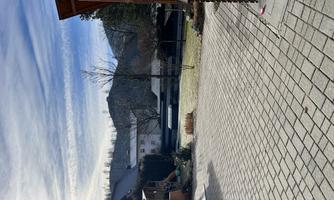 A paved courtyard overlooking a row corner house and mountains in the background. The sky is blue with a few clouds and it is daytime.
