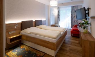 A cozy bedroom with a double bed and warm wooden furniture. The room is bright and has a television as well as a large window area with plenty of natural light.