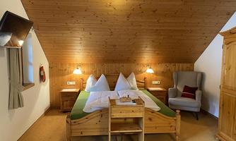 A cozy bedroom with a wooden bed and two pillows. The walls are made of wood, and an armchair is in the corner.