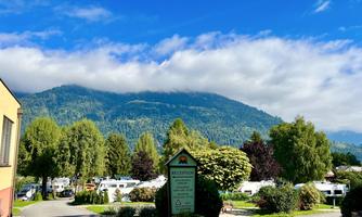 A picturesque campsite with a view of the mountains. Green trees and a clear sky create a relaxed atmosphere.