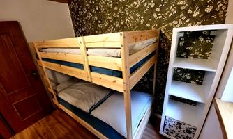 A cozy bedroom with a wooden bunk bed and a floral background wallpaper. Next to the bed is a modern, white shelf with open compartments.