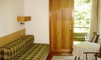 A simple living room with a padded sofa and a table. The door opens to a balcony overlooking the green outside view.