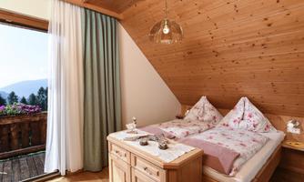 A cozy bedroom with wooden paneling and a double bed. The large French door offers a view of the nature outside.