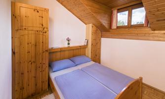 A cozy bedroom with wooden paneling. It features a double bed and a window with a view of the outdoors.