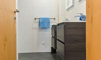 A modern bathroom with a wooden and tiled floor. There are sinks, mirrors, and blue towels on the wall.