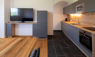 Modern kitchen with gray cabinets and wooden surfaces. A television is mounted on the wall, and the floor is made of wood and tiles.