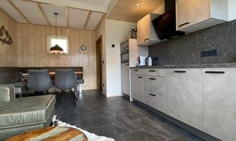 A modern kitchen with gray cabinets and a cooktop, connected to a cozy dining area. The room has bright wood and an inviting atmosphere.