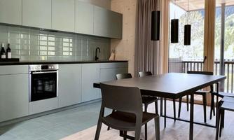 A modern kitchen with gray cabinets and a large dining table. Large windows allow plenty of light in and provide a view outside.