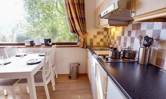 A bright kitchen with modern furniture and a dining table. Natural light streams in through the window and there are pots on the stove.