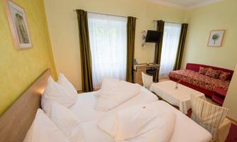 A cozy room with two beds and a red sofa. Large windows let in a lot of daylight.