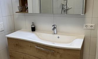 A modern bathroom with a wooden washbasin and a large mirror. The walls are light tiled, and the room feels clean and well-lit.
