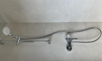 A modern shower fixture with a flexible hand shower head. The walls are brightly tiled, creating a clean atmosphere.