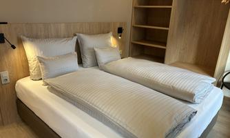 A cozy bedroom with two single beds and light bed covers. In the background, there is an open wardrobe.