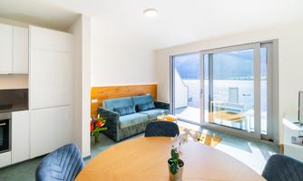 A bright, modern living and dining room with a round table and a blue sofa. Large windows offer a view of the landscape.