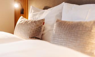 A cozy bed with soft pillows and warm light. The bedding is bright and inviting.