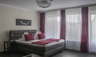 A modern bedroom with a large double bed. The windows are adorned with bright curtains and the room has a stylish atmosphere.