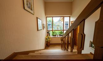 A cozy wooden staircase leads up to the rooms and holiday apartments. In the background, there is a window with a beautiful view of plants.