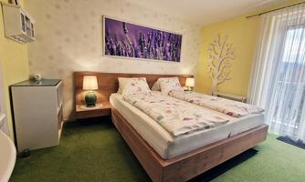 A cozy bedroom with a double bed and green carpeting. A picture of lavender hangs on the wall, and the room has a balcony with plenty of light.