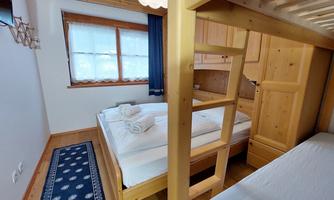 A cozy bedroom with wooden beds and a carpet. There are two beds and a large window with curtains.