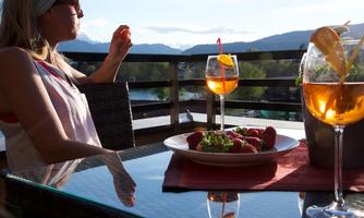 A woman sits relaxed on a balcony and enjoys a drink. Fresh strawberries and a salad are on the table.