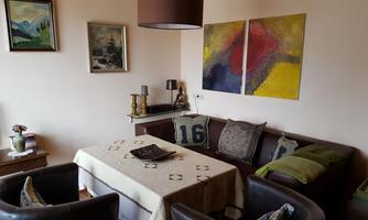 A cozy living room with a sofa, a table, and various artworks on the wall. The decor is modern and inviting, with colorful accents.