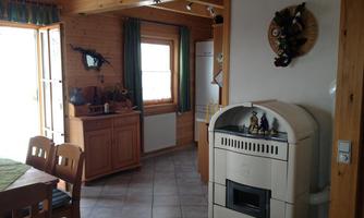 A cozy room with wooden furniture and a stove. The window offers plenty of daylight and looks outside.