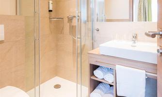 A modern bathroom with a walk-in shower and an elegant sink. The walls are in a soft beige, and fresh towels are neatly stored.