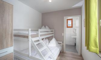 A cozy room with a bunk bed and bright walls. In the background, a bathroom is visible.