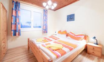 A cozy bedroom with a large bed and colorful bedding. The room has wooden floors and a desk with a lamp.