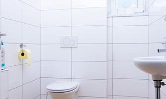 A modern bathroom with white tiles. There is a toilet and a sink.