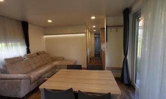 A modern living room with a comfortable sofa and a dining area. Large windows provide plenty of daylight.