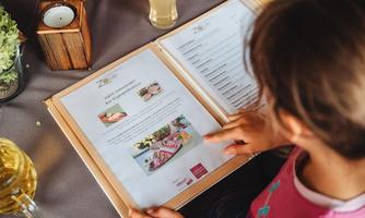 A child is reading the menu in a restaurant. The menu features various dishes and images.