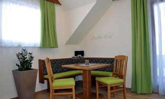 A cozy dining area with a wooden table and chairs in a bright room. Green curtains and a plant give the room a fresh atmosphere.