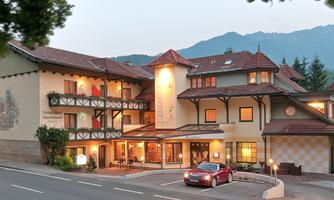 A charming hotel with a traditional design and an inviting entrance. Majestic mountains can be seen in the background.